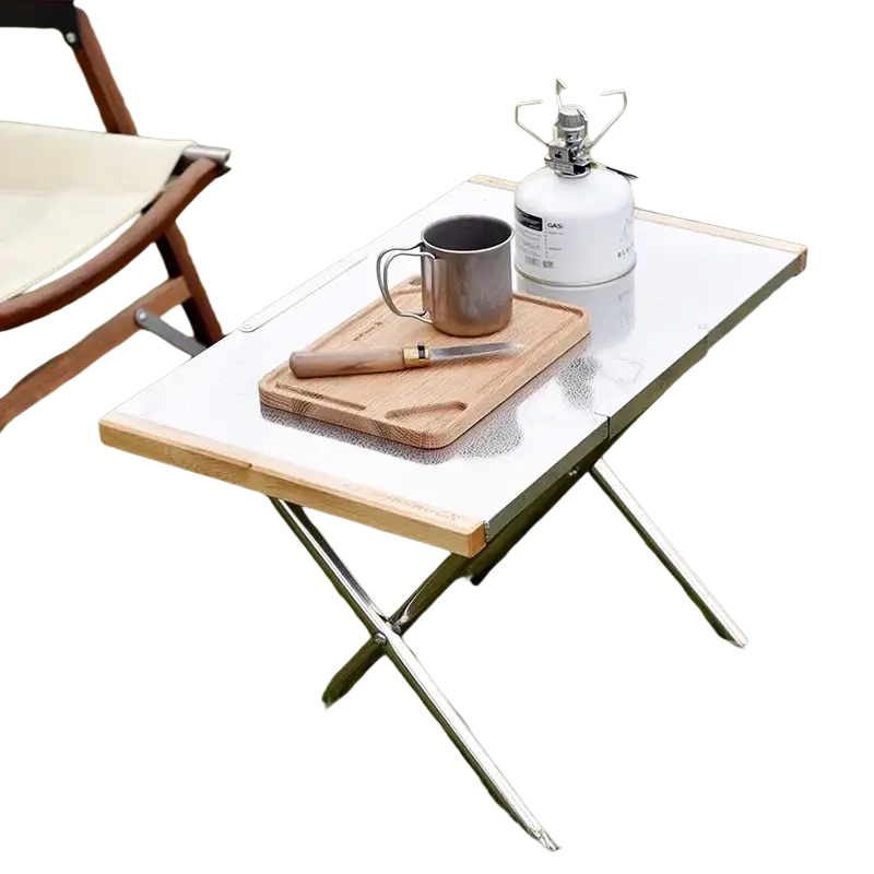 A sleek stainless steel camping table with white metal surface, light wood edges, chrome legs, and storage bag for outdoor furniture