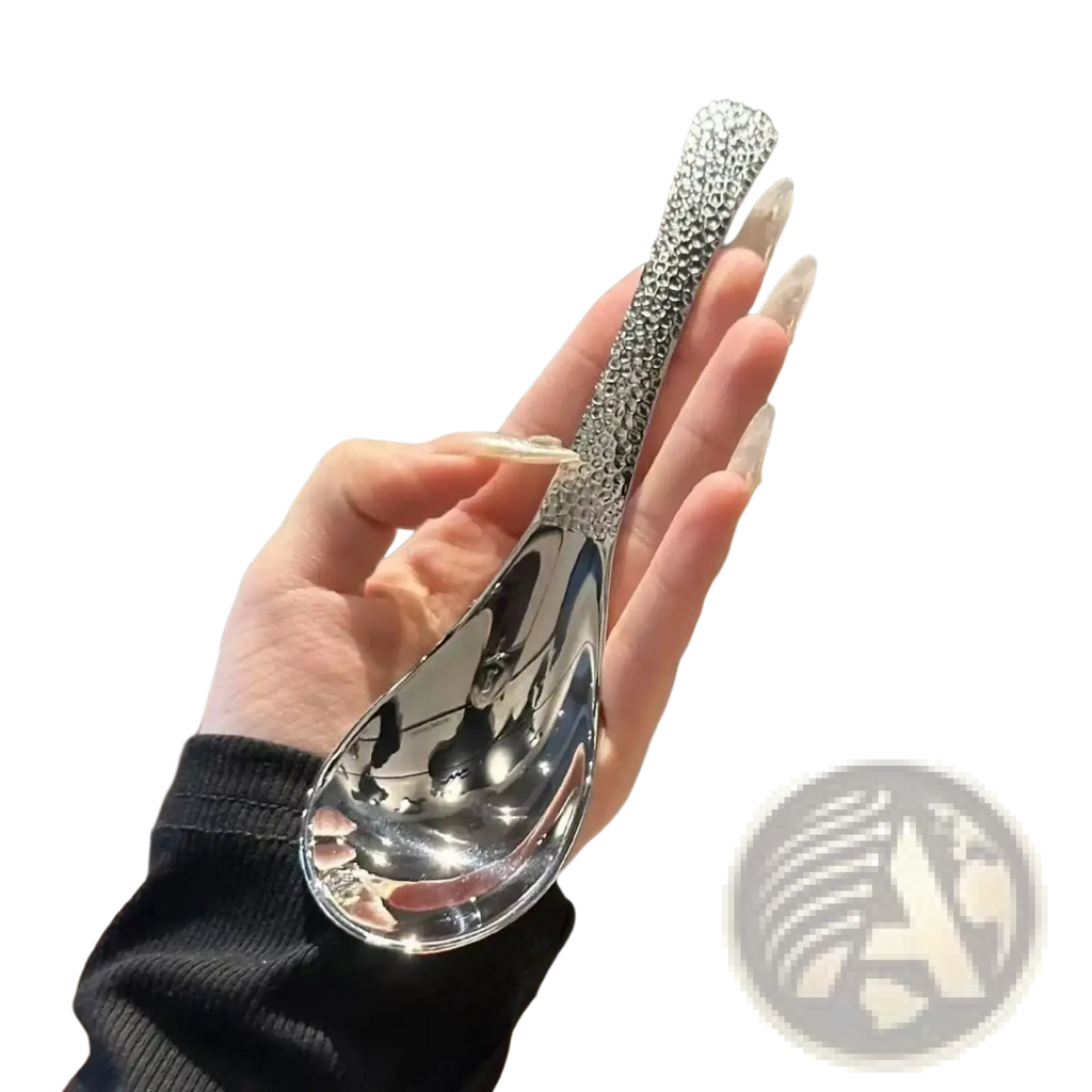 A sleek silver stainless steel dessert spoon with a textured beaded handle and polished reflective bowl