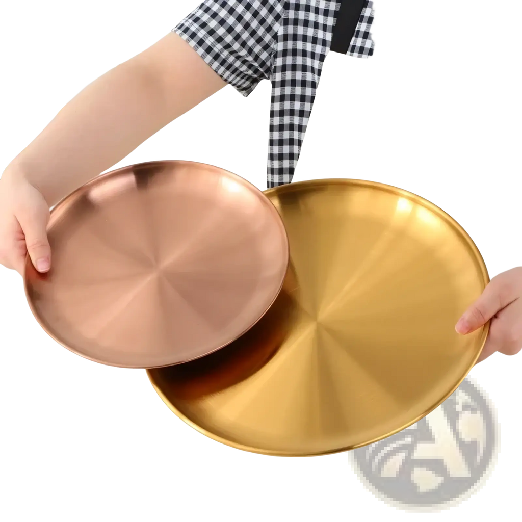 Two round metallic stainless steel dinner plates with brushed copper and gold finish held by hands in apron