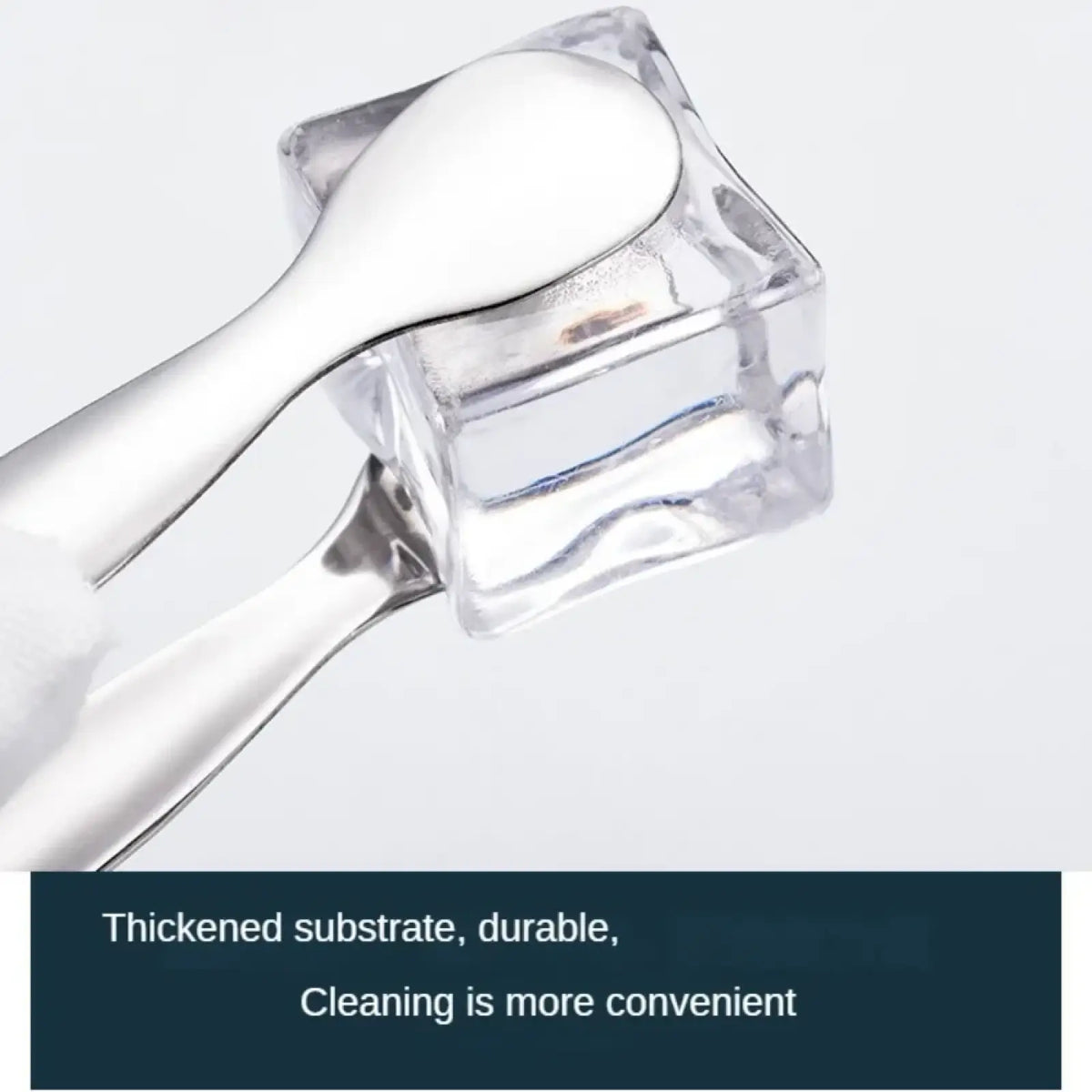 A sleek silver stainless steel mini ice tong with a smooth bowl and slender handle on a glass container