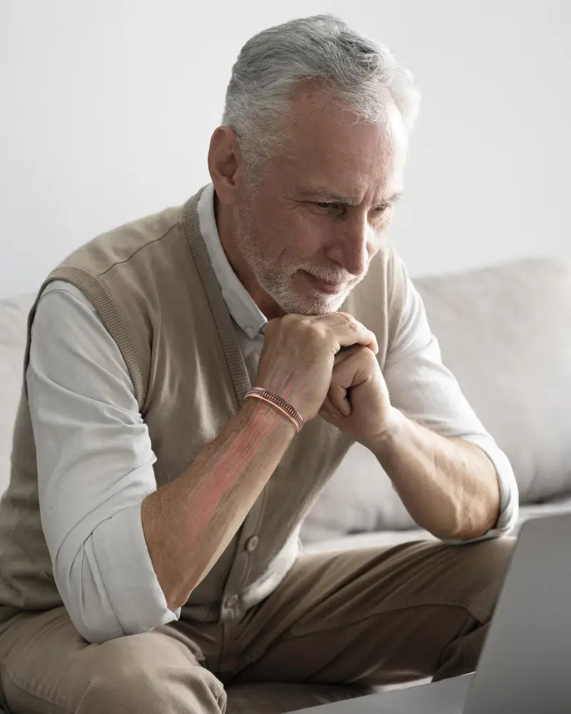 A man with gray hair and beard wearing beige vest showcases a handcrafted pure copper magnetic therapy bracelet for men