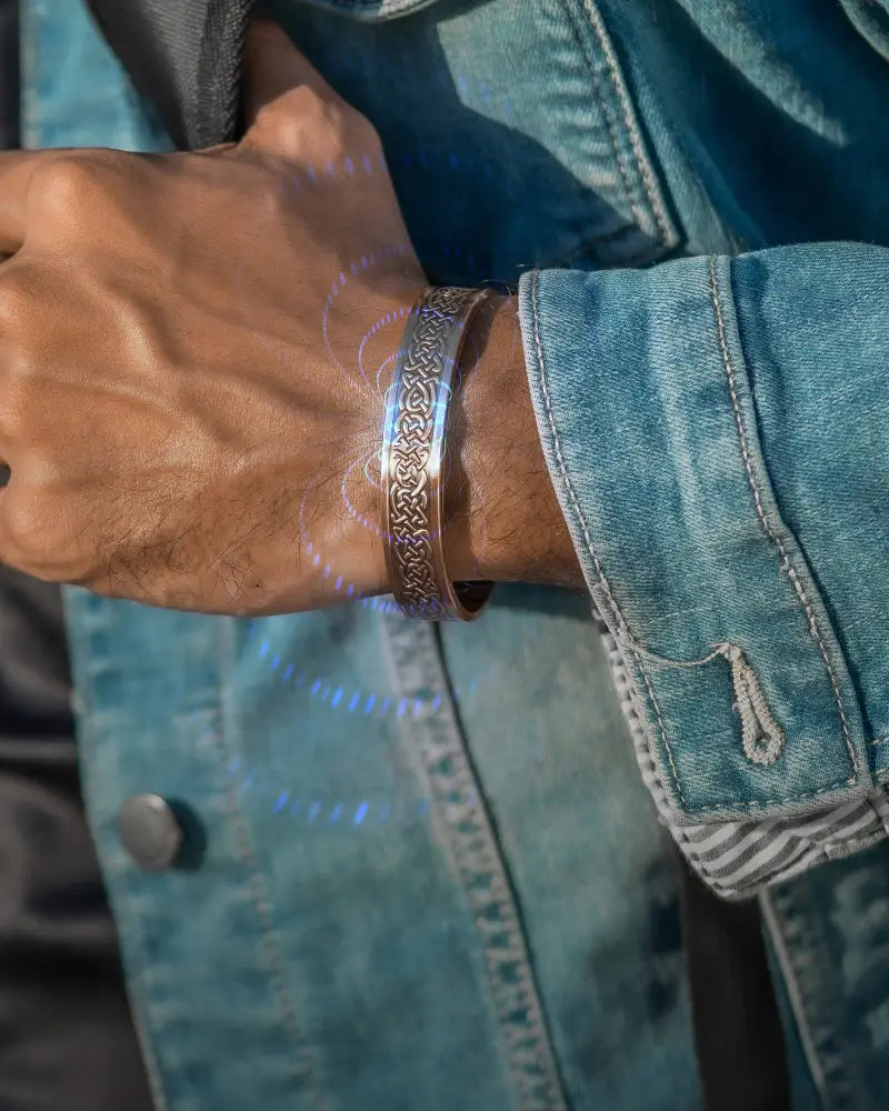 A silver-toned intricately engraved bangle bracelet worn on a wrist with rose gold shielded knot magnetic copper for men