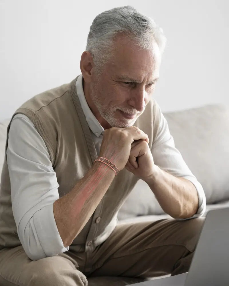 A man with gray hair and beard wearing a beige knitted vest modeling a viking stamped magnetic copper cuff bracelet for men