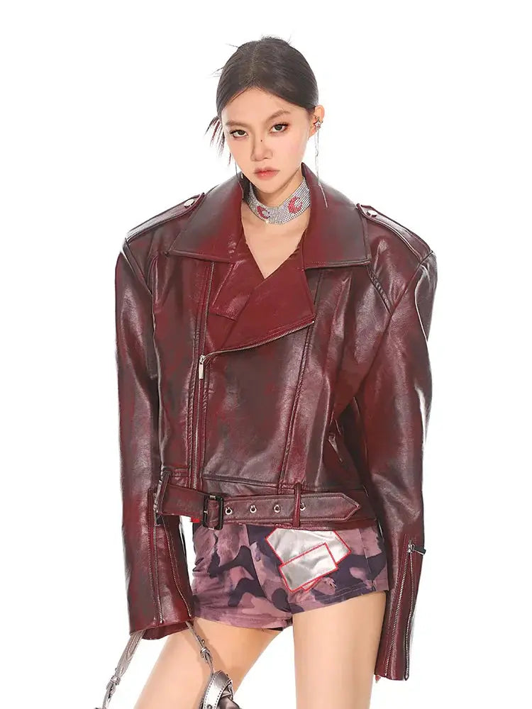 Glossy burgundy leather moto jacket with a stand collar, belted waist, and asymmetrical zipper detail