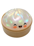 A cute iridescent steamed bun squeezing toy with smiling face and rosy cheeks in a steamer container
