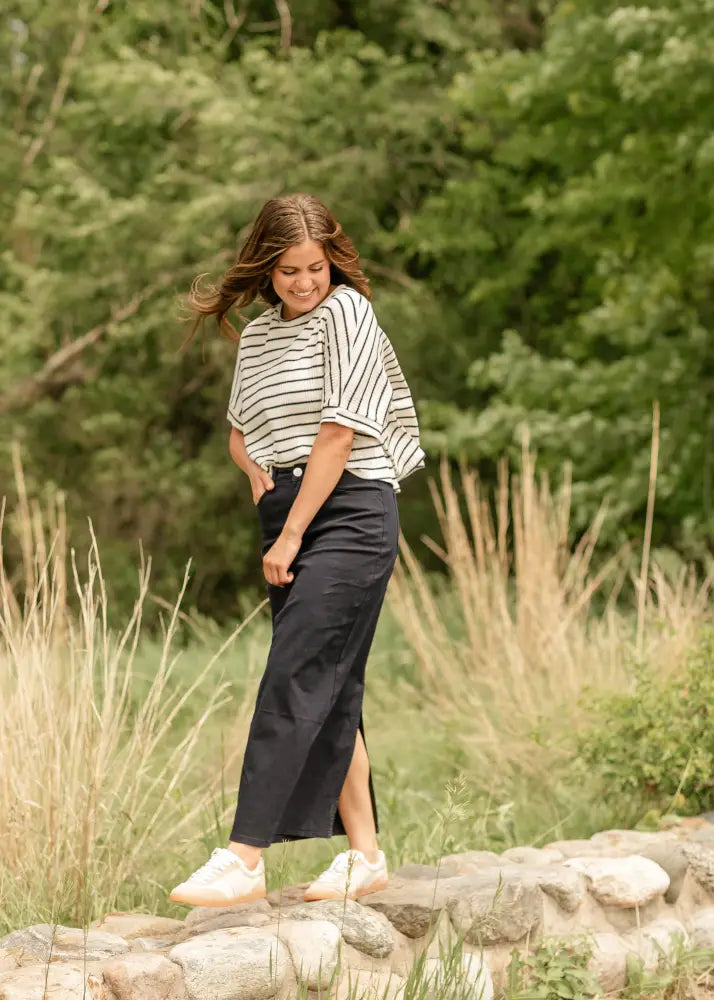 A woman wears a black and white striped short-sleeved top with a relaxed fit and a Stella navy embroidered maxi denim skirt with back slit
