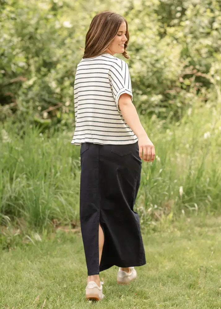 A woman wearing a black and white striped top with the back side of a stella navy embroidered maxi denim skirt with back slit