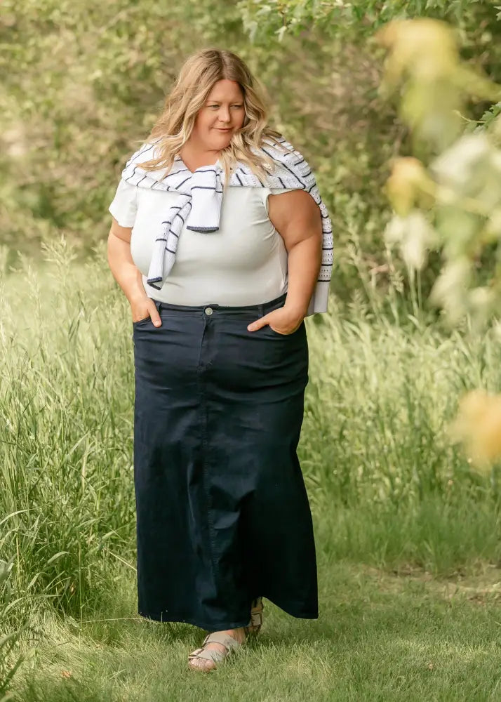 A woman wearing a white top with a striped scarf paired with the stella navy embroidered maxi denim skirt with back slit visible from the back