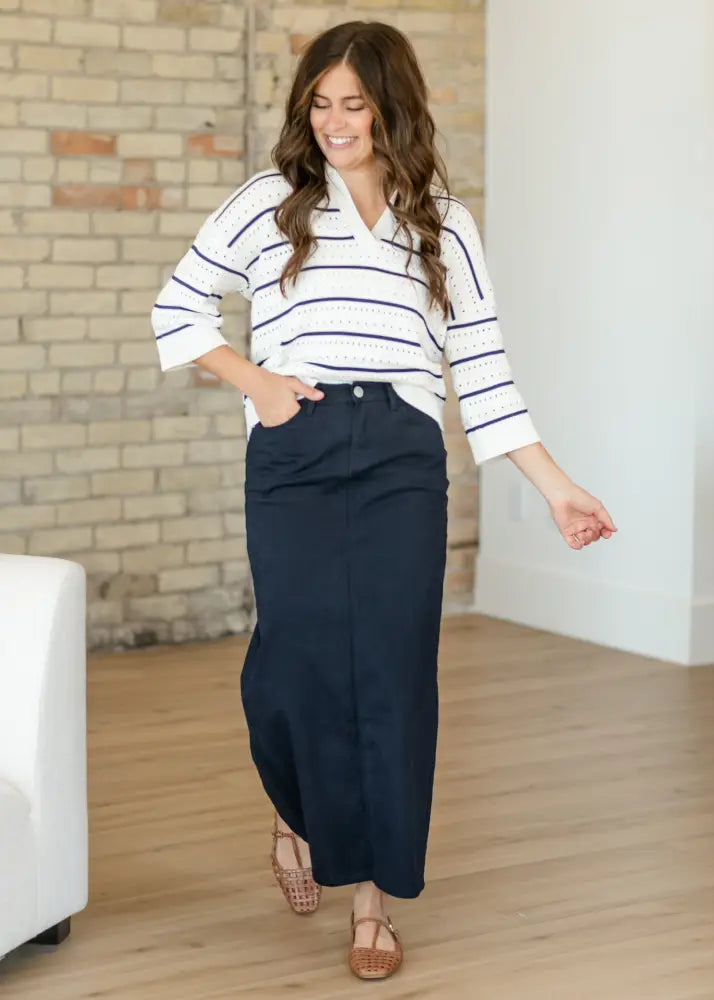 A woman wears a white and navy blue striped top paired with a dark navy embroidered maxi denim skirt with back slit