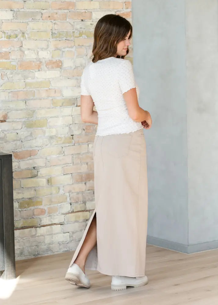 A woman wears a white lace short sleeve top with beige wide leg trousers and a taupe high waisted denim maxi skirt