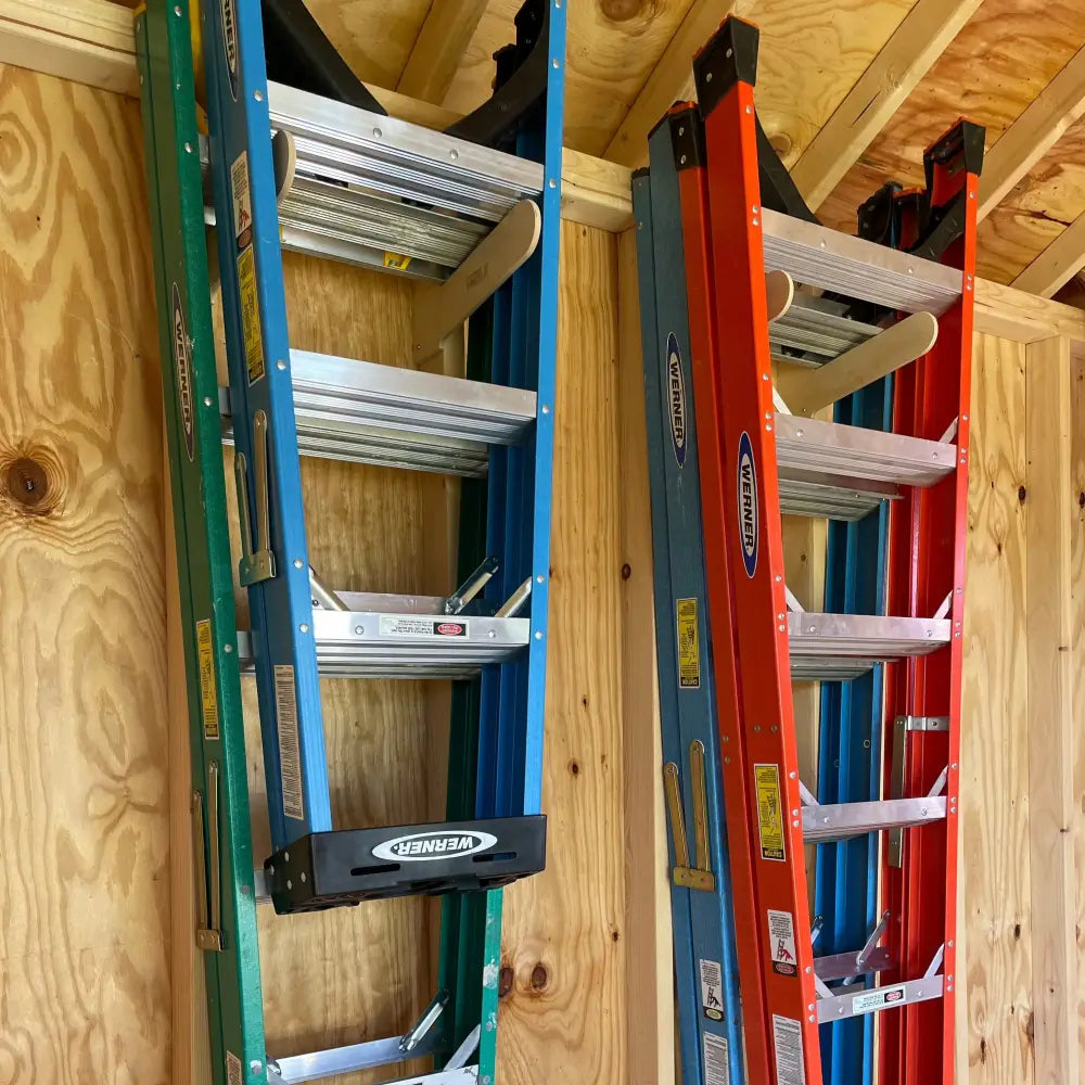 Two werner brand heavy duty birch plywood dual step ladder wall racks holding green blue and red gray aluminum alloy ladders