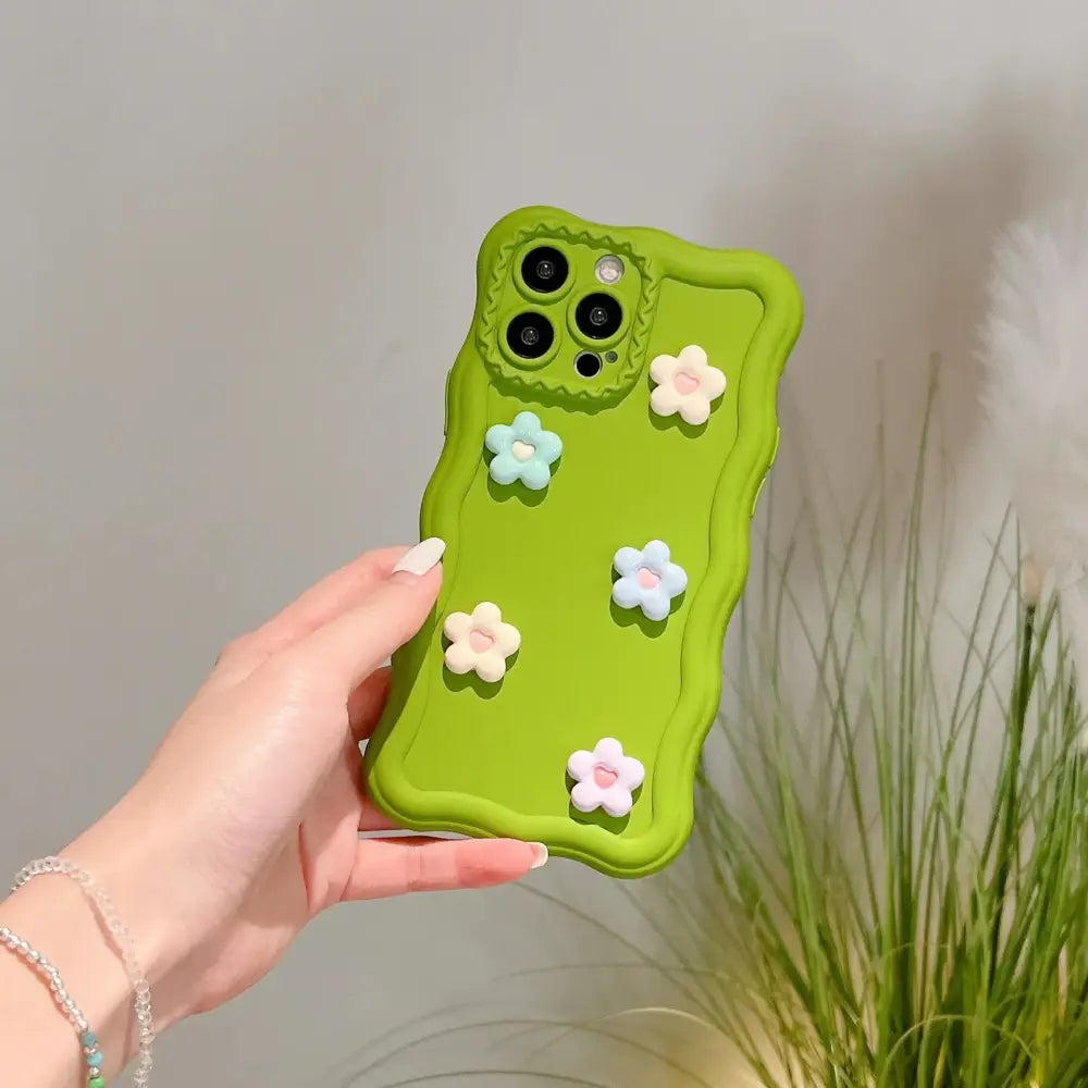 A lime green silicone phone case with five pastel-colored 3d flower charms on the back side