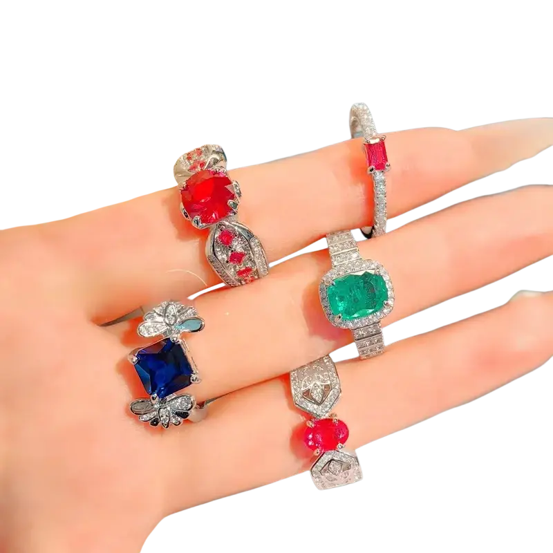 A hand displays sterling silver ruby gemstone rings with intricate diamond-encrusted designs for women