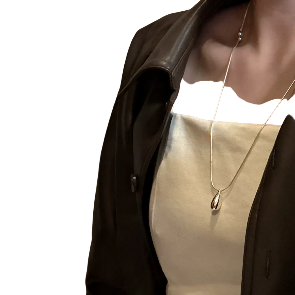 Sterling silver teardrop necklace with a sleek silver minimalist pendant worn with a cream top and leather jacket