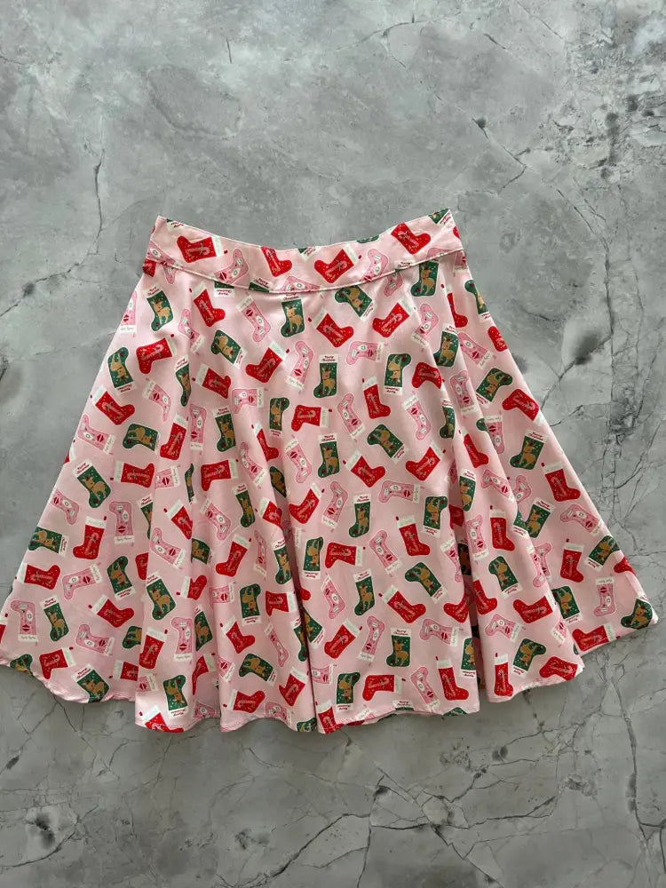 Pink cotton skater skirt with a festive pattern of red and green christmas stockings featuring a flared design