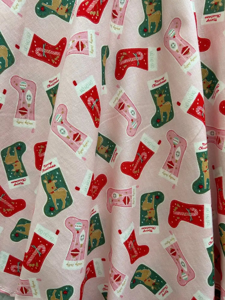 Pink cotton skater skirt featuring festive red and green christmas stockings with reindeer candy canes and merry christmas text