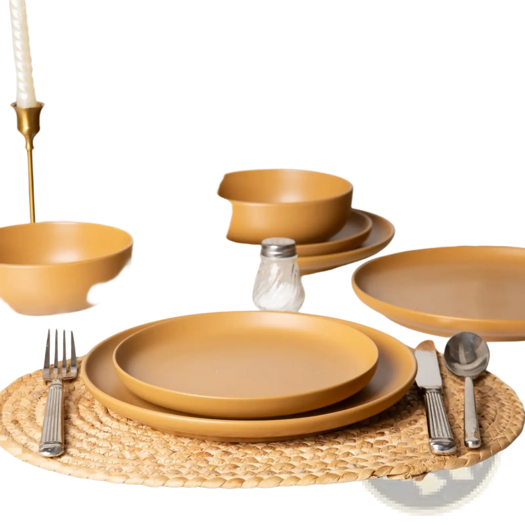 Warm mustard-yellow stoneware dinnerware set with matte glaze includes bowls plates and cutlery on a woven placemat