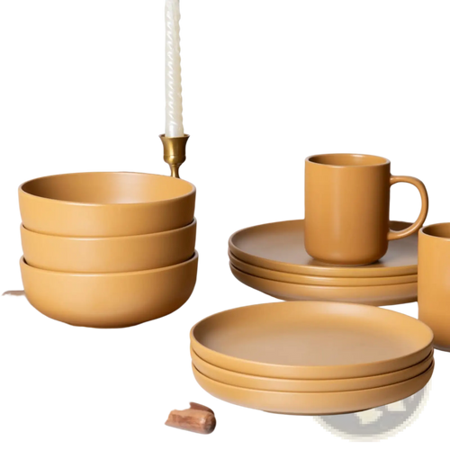 Set of 12-piece matte glaze mustard-yellow stoneware dinnerware with bowls plates and mugs on wooden surface