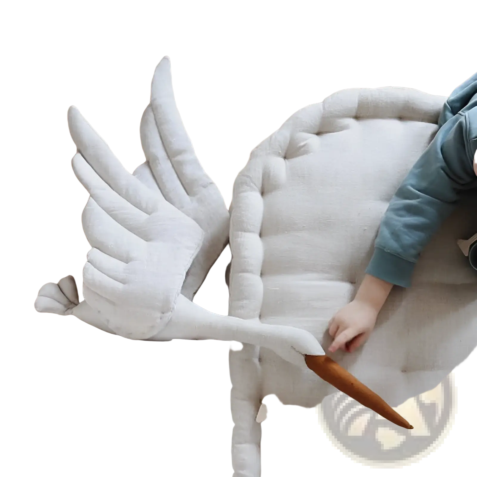 White plush stork-shaped pillow with quilted wings and tufted body resting on wooden floor beside child’s hand