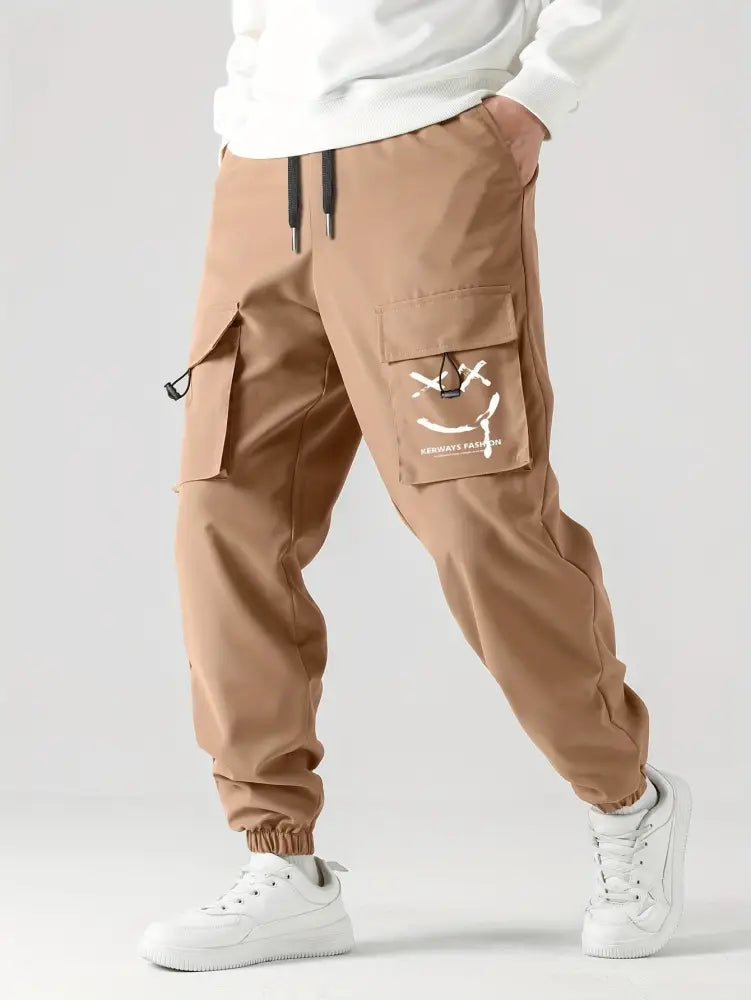 Men’s tan tactical wear resistant cargo joggers with multiple pockets and a white smiley face graphic on the thigh