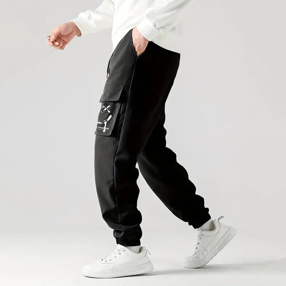 Men’s black wear resistant cargo joggers featuring a large side pocket with a white graphic design