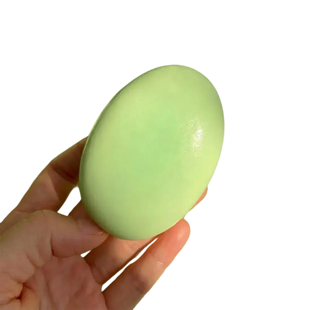 A hand holds a smooth pale green stress relief slow rising cheese cake squishy toy with a glossy surface