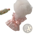 A fluffy white dog wearing a pink and white striped ruffled satin princess dog dress with bow at the back