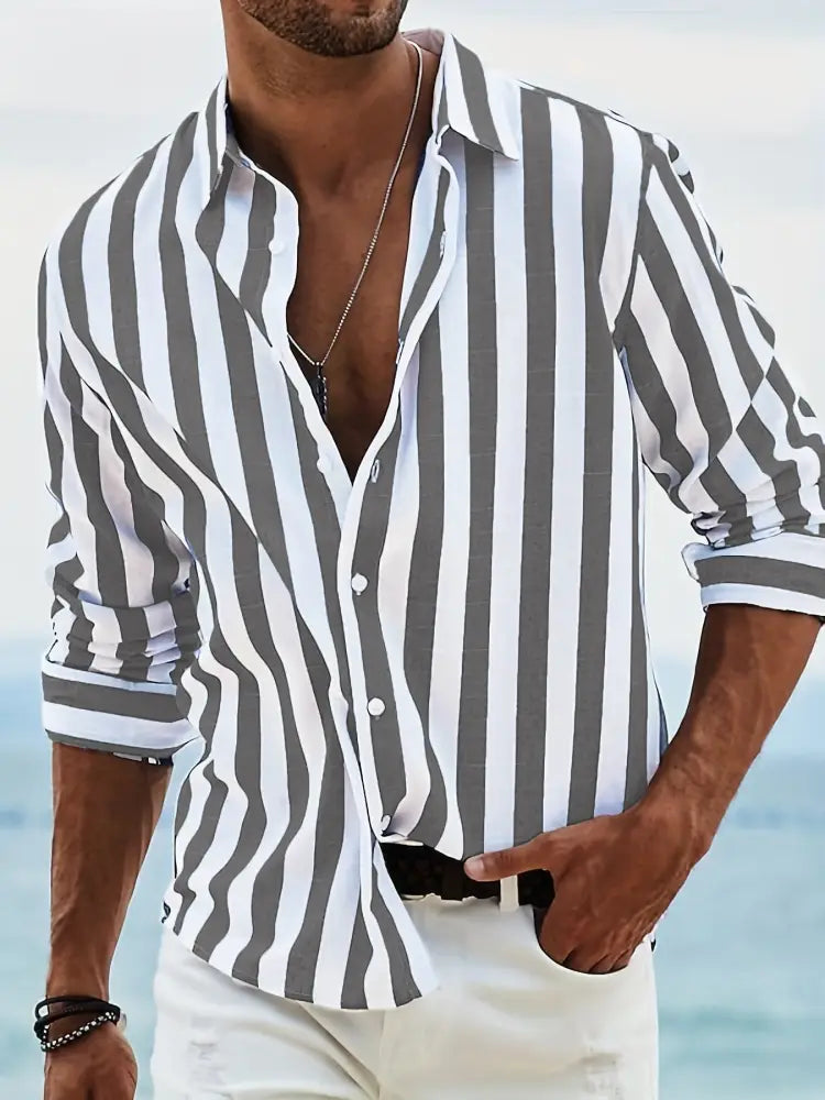 A man wearing a men’s loose fit vertical striped gray and white long sleeve casual button-down shirt with rolled sleeves