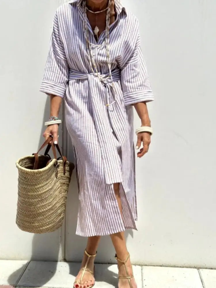 A woman wears a lavender and white striped linen belted lapel shirt dress with three-quarter sleeves and a front slit