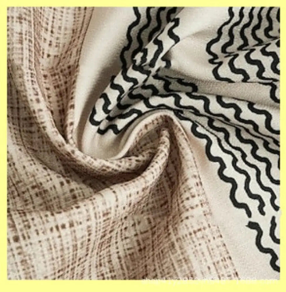 A soft cream-colored scarf with a textured weave and bold black wavy lines paired with a men’s striped slub linen shirt