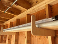 Stud mounted wood and pipe shed storage hooks with white pvc pipe and black fittings on a wooden shelf