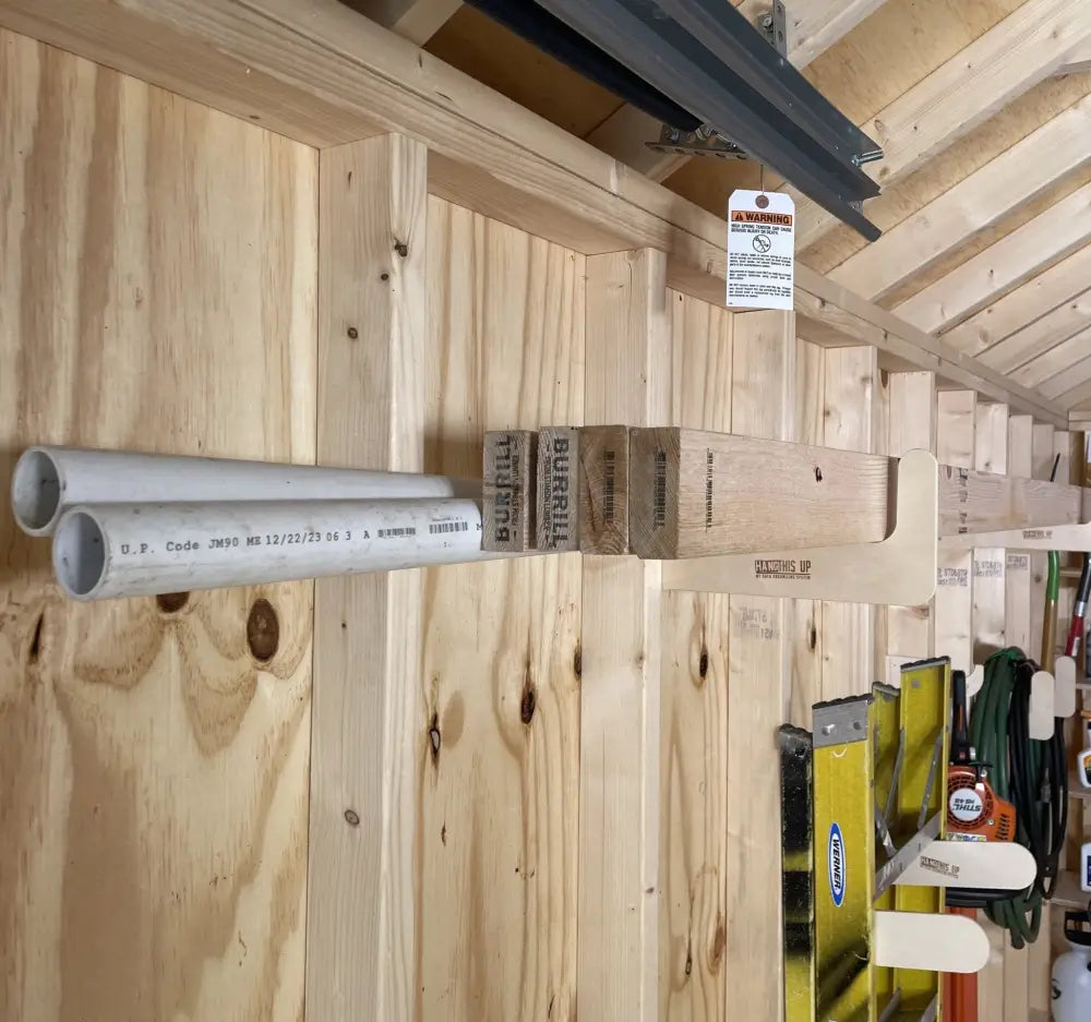 Silver-colored pvc pipes mounted horizontally on wooden wall in stud mounted wood and pipe shed storage hooks product