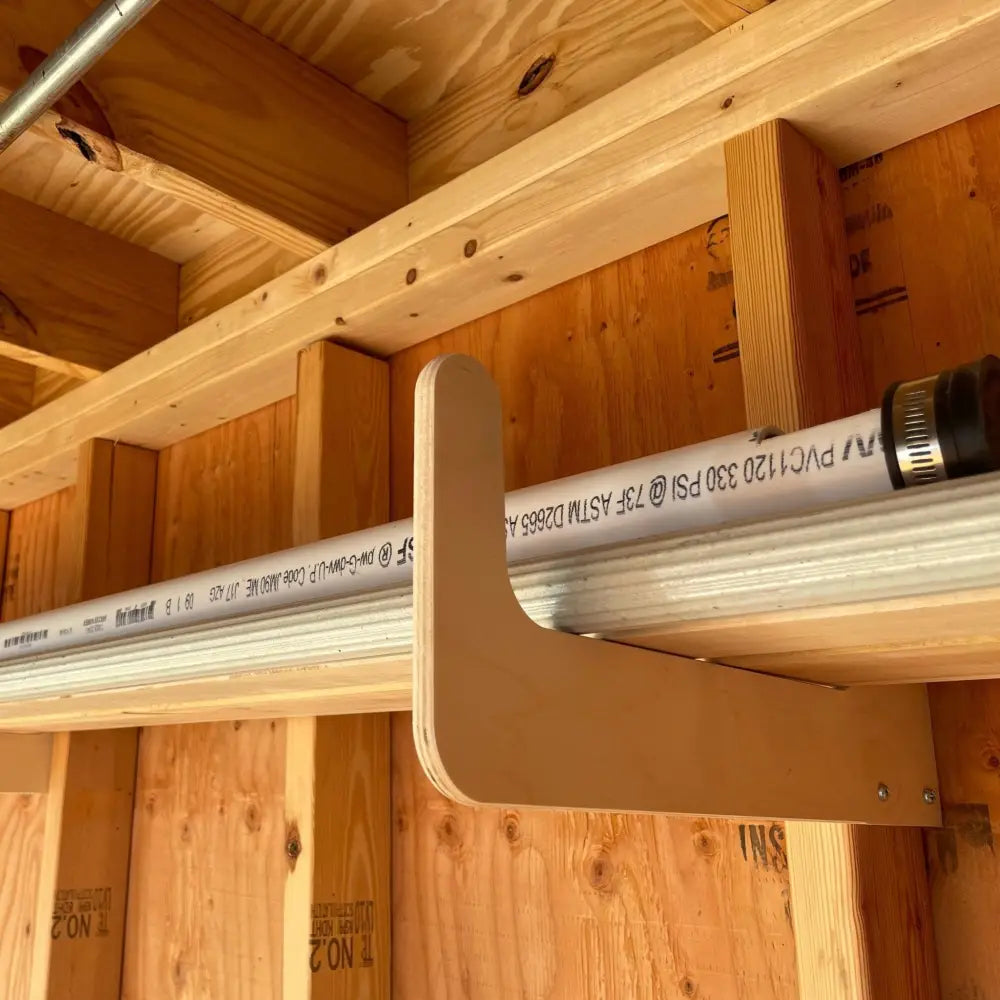 Light-colored wooden stud mounted pipe rack holding white pvc pipe with black text and metal fitting for shed storage hooks