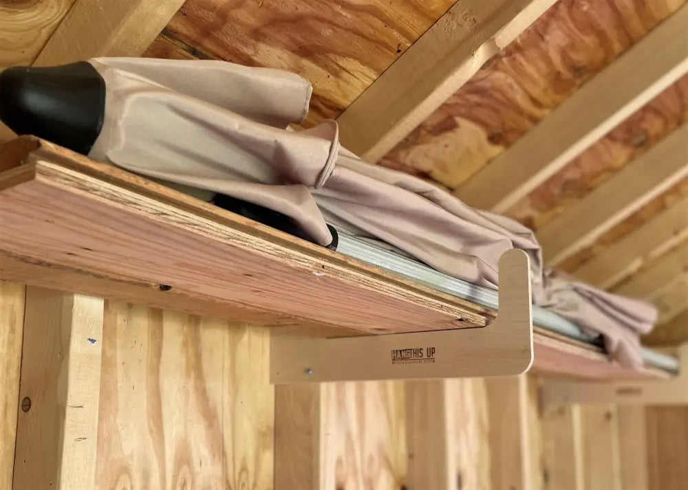 Beige and black umbrella stored on wooden shelf with stud mounted wood and pipe shed storage hooks