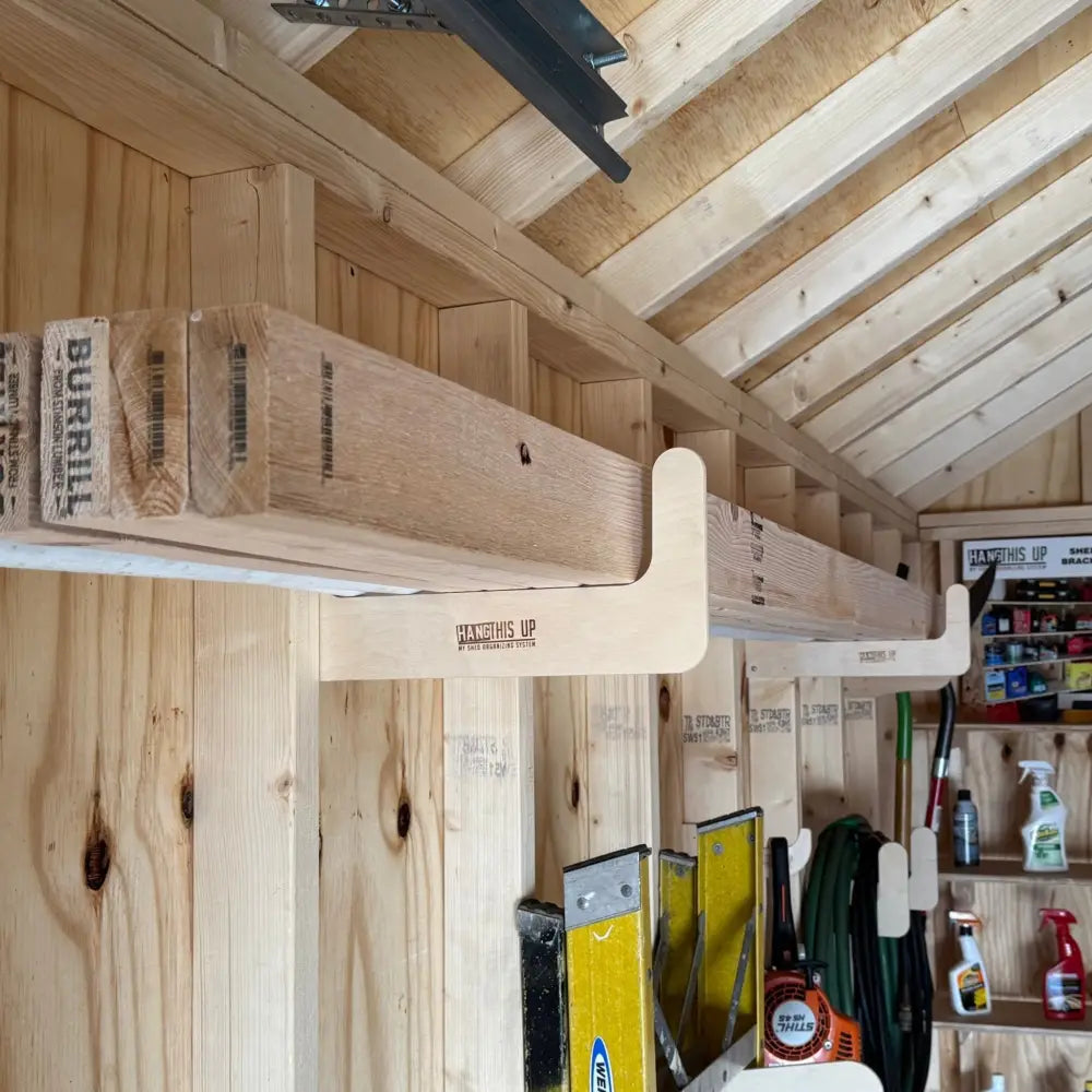 Light-colored wooden stud mounted wood and pipe shed storage hook with curved end and hang this up engraving holding lumber