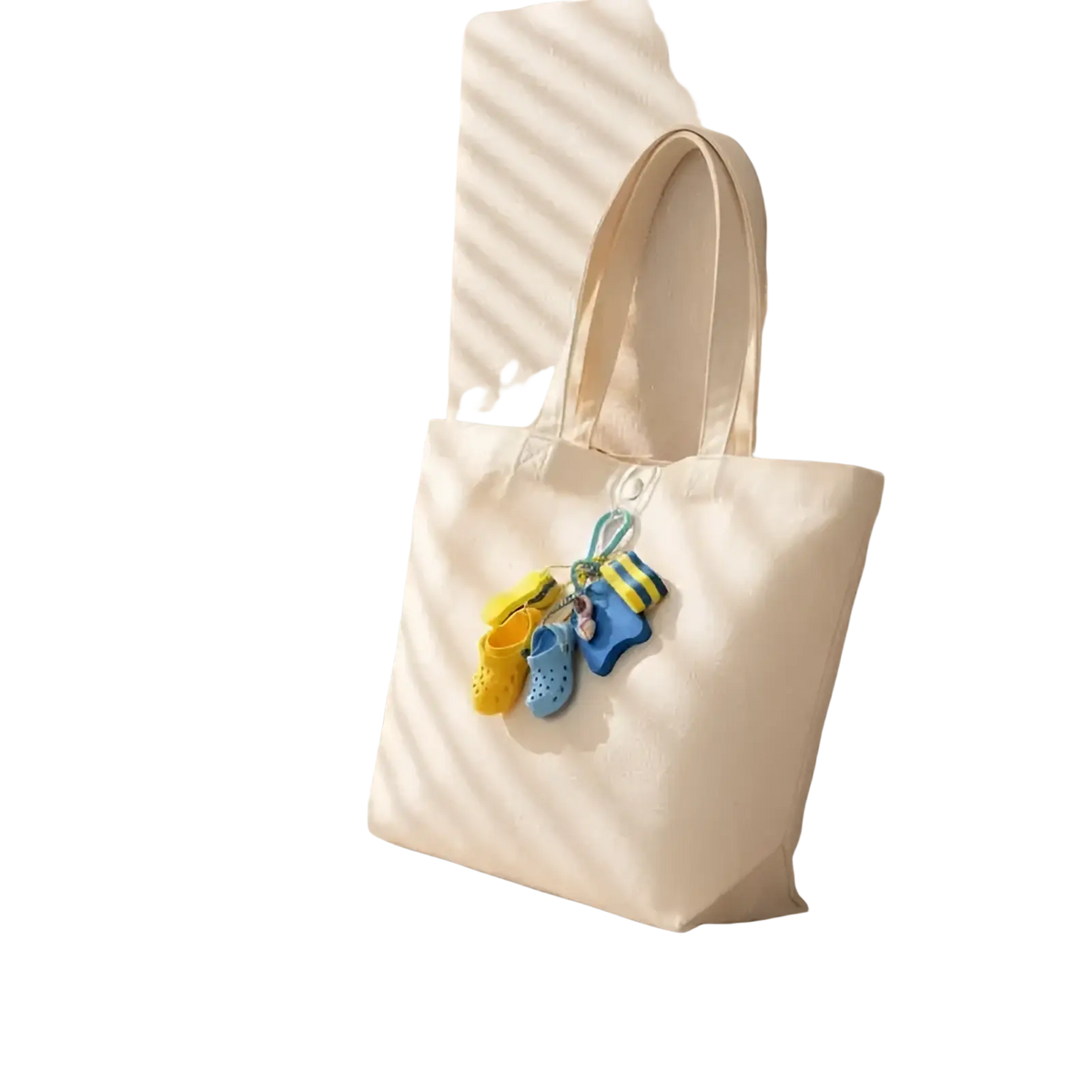 Cream-colored canvas tote bag with matching handles featuring colorful yellow and blue summer beach clog keychain charms