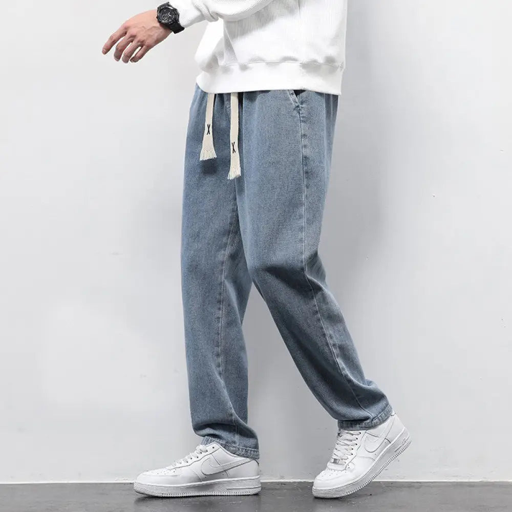 Men’s wide leg light wash denim joggers with a drawstring waist and frayed hem in light-wash denim