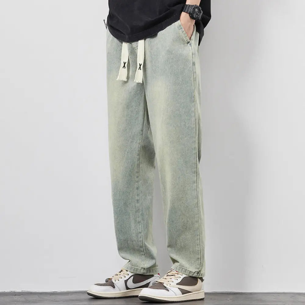Men’s wide leg light wash denim joggers with white drawstrings and black x logos in light-wash denim fabric