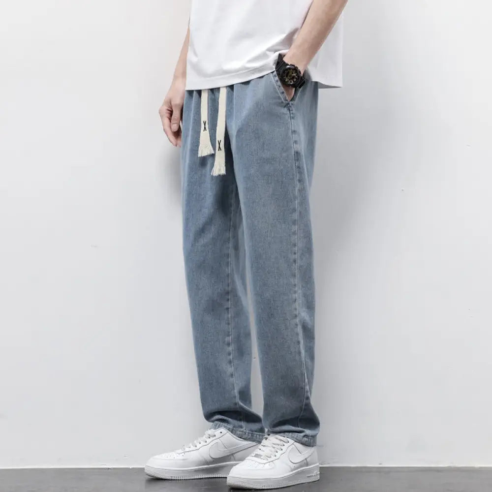 Men’s wide leg light wash denim joggers with white drawstrings and black x embroidery on light-wash fabric