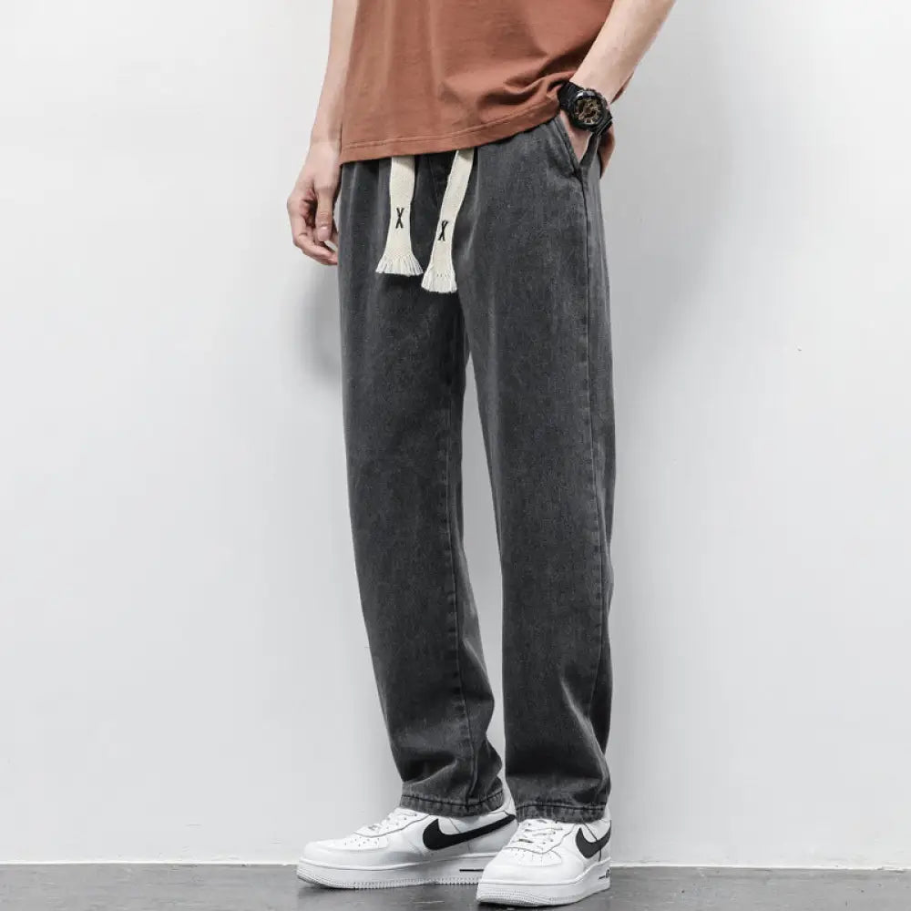 Men’s wide leg dark gray denim joggers with white drawstring ties and black x lettering on light wash material