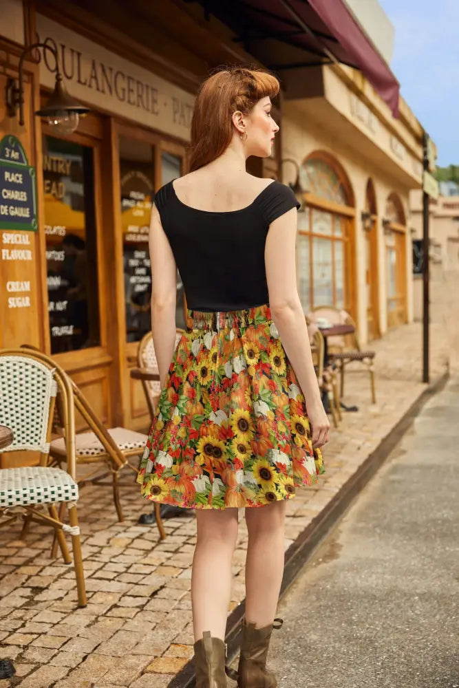A woman wearing a sunflower and pumpkin autumn floral skater skirt with black short-sleeved top