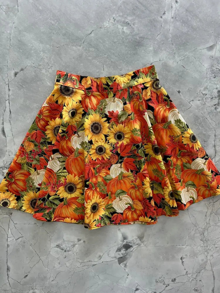 A vibrant autumn-themed pleated skater skirt with orange pumpkins sunflowers and red leaves on black background