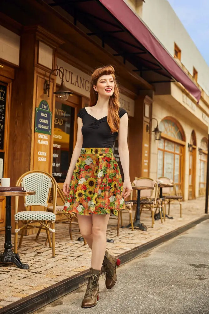 A woman wears a sunflower and pumpkin autumn floral skater skirt with vibrant yellow and orange blossoms paired with a black top