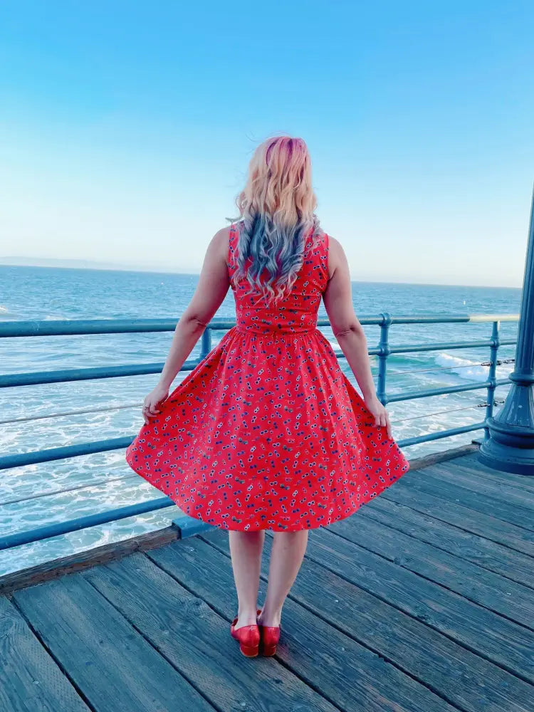 A vibrant red floral print cotton a-line dress with fitted bodice and flared skirt worn on a wooden pier