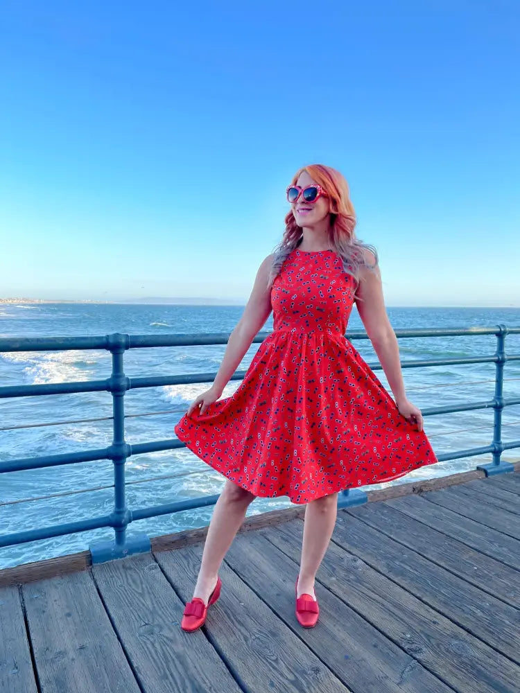 A vibrant red sleeveless cotton a-line dress with floral sunglasses print and a fitted bodice