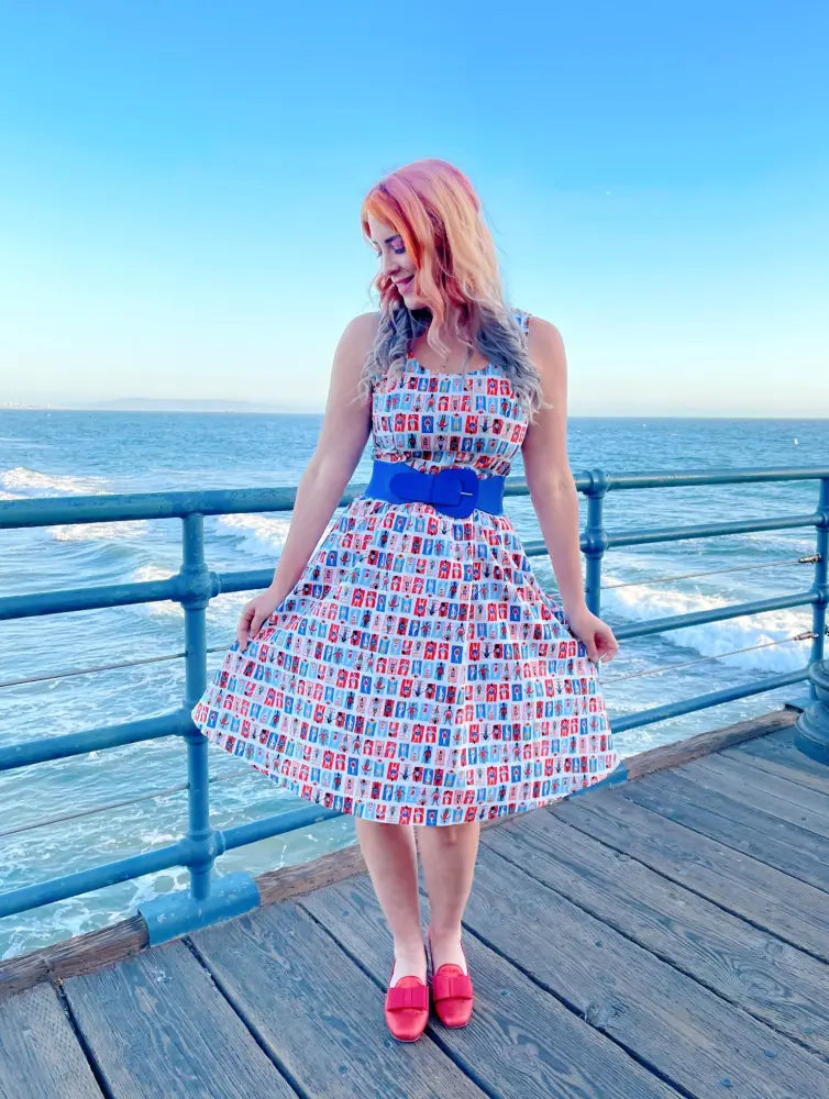 A woman wears a sleeveless sunny days vintage house print fit and flare dress with a royal blue waist belt