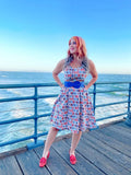 A woman wearing a sleeveless sunny days vintage house print fit and flare dress with red and blue rectangular patterns on white