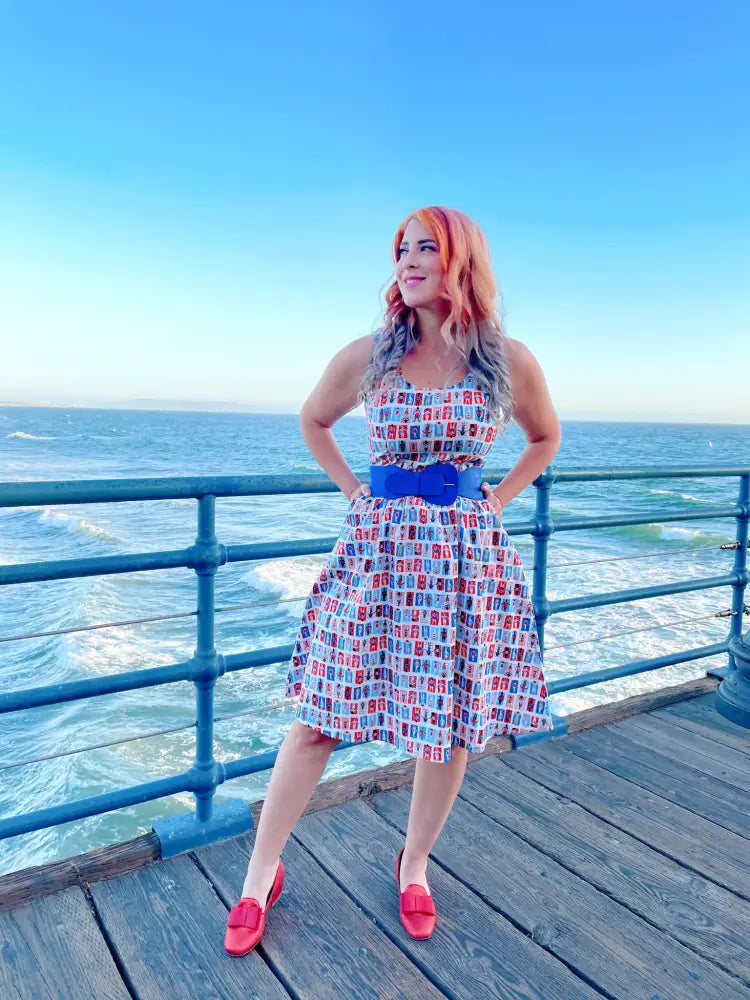 A woman wearing a sleeveless sunny days vintage house print fit and flare dress with red and blue rectangular patterns on white