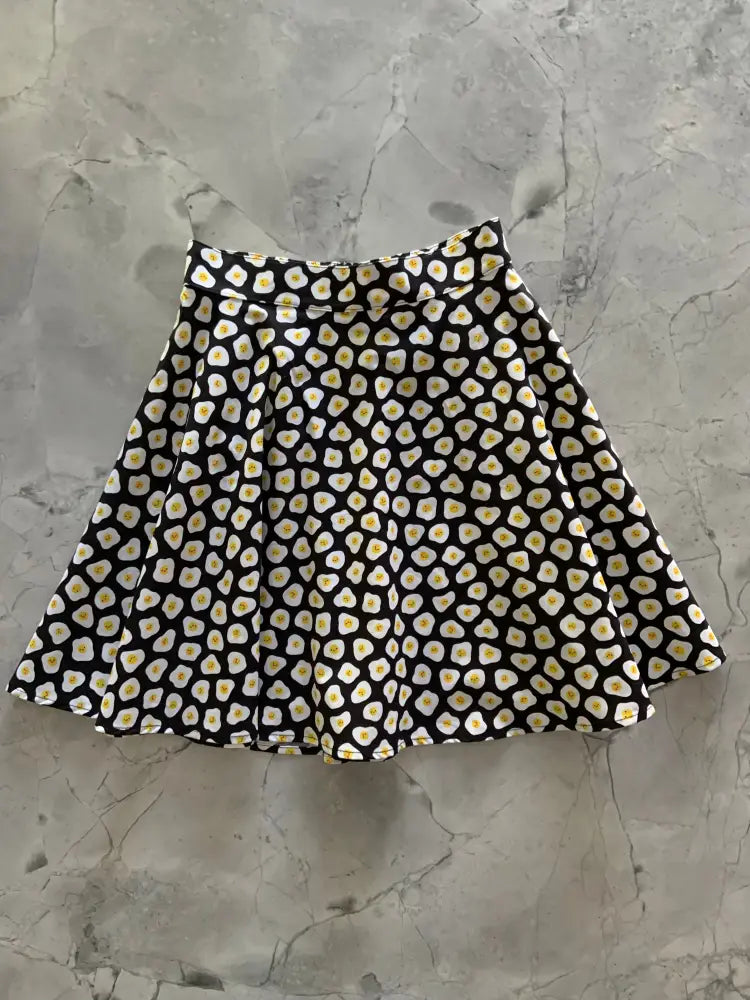 Black pleated skirt with a repeating pattern of white and yellow fried egg motifs called sunny side up polka dot skater skirt