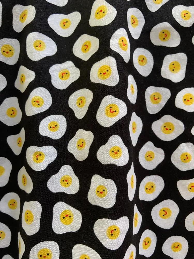 Black fabric sunny side up polka dot skater skirt with repeating white cartoon fried eggs smiling yellow yolks pattern